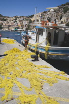 Yialos harbour  the main port of Symi island.  Blue and white painted fishing boat moored beside jetty with yellow fishing nets spread out across stone surface.AegeanGreek IslandsSimicoast coastal...