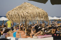 Yialos.  Sunbathers on crowded beach under thatched sunshade looking out over sea.AegeanGreek IslandsSimicoast coastalseaSummerpackageholidayresortvacationtripdestinationDestinations Ella...