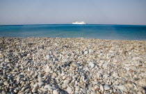 Yialos.  Stretch of empty pebble beach across calm  aquamarine water towards cruise ship on horizon.AegeanGreek IslandsSimicoast coastalseaSummerpackageholidayresortvacationtripdestination...