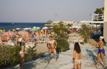 Yialos.  Group in swimwear playing volleyball beside busy beach crowded with striped sun umbrellas and loungers.AegeanGreek IslandsSimicoast coastalseaSummerpackageholidayresortvacationtrip...
