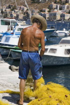 Yialos.  Fisherman working with bright yellow nets on the harbourside with moored boats beyond.AegeanGreek IslandsSimicoast coastalseaSummerpackageholidayresortvacationtripdestinationDest...