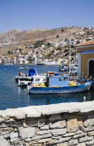 Yialos.  Blue and white painted fishing boats and pleasure craft moored in harbour with waterfront buildings beyond.AegeanGreek IslandsSimicoast coastalseaSummerpackageholidayresortvacation...