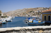 Yialos.  Blue and white painted fishing boats and pleasure craft moored in harbour with waterfront buildings beyond.AegeanGreek IslandsSimicoast coastalseaSummerpackageholidayresortvacation...