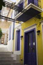 Yellow  purple and white painted facade of house with balcony and window shutters on narrow street with flight of stone steps. AegeanGreek IslandsSimicoast coastalseaSummerpackageholidayresor...