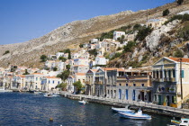 Yialos.  Waterfront buildings overlooking moored boats with houses extending over steep  rocky hillside behind.AegeanGreek IslandsSimicoast coastalseaSummerpackageholidayresortvacationtrip...