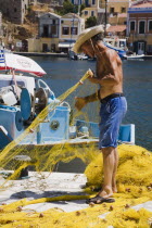 Yialos.  Fisherman working with bright yellow nets on the harbourside with moored boats behind.AegeanGreek IslandsSimicoast coastalseaSummerpackageholidayresortvacationtripdestinationDest...