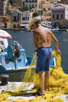 Yialos.  Fisherman working with bright yellow nets on the harbourside with moored boats behind.AegeanGreek IslandsSimicoast coastalseaSummerpackageholidayresortvacationtripdestinationDest...