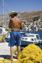 Yialos.  Fisherman working with bright yellow nets on the harbourside with moored boats behind.AegeanGreek IslandsSimicoast coastalseaSummerpackageholidayresortvacationtripdestinationDest...