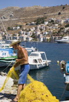 Yialos.  Fisherman working with bright yellow nets on the harbourside with moored boats behind.AegeanGreek IslandsSimicoast coastalseaSummerpackageholidayresortvacationtripdestinationDest...