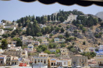 Yialos.  Pastel coloured town houses extending over rocky hillside scattered with trees.AegeanGreek IslandsSimicoast coastalseaSummerpackageholidayresortvacationtripdestinationDestination...
