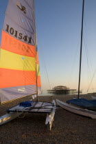 Hobbie Cat sailing catamaran dingy on the beach with colourful sail aloft. Shell of the former West Pier can be seen on the horizon.Colorful European Great Britain Holidaymakers Northern Europe Sand...