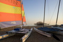 Hobbie Cat sailing catamaran dingy on the beach with colourful sail aloft. Shell of the former West Pier can be seen on the horizon.Colorful European Great Britain Holidaymakers Northern Europe Sand...