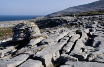 A single boulder sits in a limestone section with the slops of Slieve Elva and Atlantic Ocean behind.Eire European Irish Northern Europe Republic Ireland Poblacht na hEireann Blue Gray Karst Sedimen...