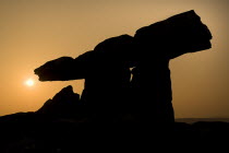 Poulnabrone Dolmen  Silhouetted against sunset. The thin capstone sits on two 1.8 metre  6 feet  high portal stones. These stones created a chamber within which the dead were placed. The people buried...