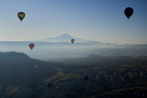 Turkey, Cappadocia, Goreme, Hot air balloons in flight over landscape, Early morning with hot air balloons in flight, Mount Erciyes in the background.