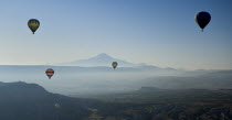 Turkey, Cappadocia, Goreme, Hot air balloons in flight over landscape with distant mountains.