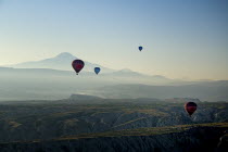 Turkey, Cappadocia, Goreme, Hot air balloons in flight over landscape, Early morning with hot air balloons in flight, Mount Erciyes in the background.