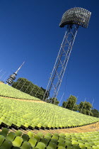 Germany, Bavaria, Munich, Olympic Stadium, The colourful green seats in the stadium with the Olympic Tower and floodlights behind.