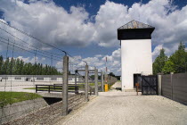 Germany, Bavaria, Munich, Dachau World War II Nazi Concentration Camp Memorial Site, fence with watch tower and reconstructed prisoner barracks.