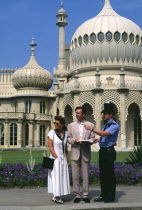 England, East Sussex, Brighton, Old Steine Young tourist couple outside the Royal Pavilion with its onion domes asking a policeman for directions.