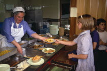 England, East Sussex, Brighton, Young girl collecting her hot meal from dinner lady ay counter in school canteen.