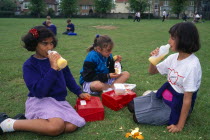 England, East Sussex, Brighton, Young girls having their packed lunches on the grass of the school playing fields.