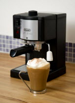 Food And Drink, Hot Drinks, Coffee, Domestic De Longhi Coffee machine on wooden kitchen worktop with a cup of cappuccino in a glass mug.