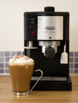 Food And Drink, Hot Drinks, Coffee, Domestic De Longhi Coffee machine on wooden kitchen worktop with a cup of cappuccino in a glass mug.