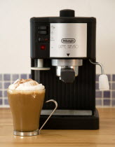 Food And Drink, Hot Drinks, Coffee, Brighton Domestic De Longhi Coffee machine on wooden kitchen worktop with a cup of cappuccino in a glass mug.