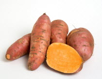 USA, Food, Root Vegetables, Group shot of North American sweet potatoes on a white background with one potato cut in half to show the orange interior.