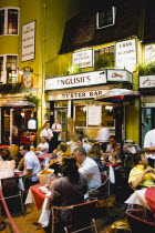 England, East Sussex, Brighton, The Lanes English's Oyster Bar and Seafood Restaurant exterior at night with people sitting outside at tables eating a meal under a patio heater.