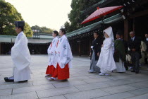 Japan, Tokyo, Yoyogi, Meiji Jingu shrine, a wedding party led by a shinto priest and two woman attendants , bride in traditional white wedding kimono, groom in traditional kimono, both about thirty ye...