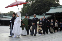 Japan, Tokyo, Yoyogi - at Meiji Jingu shrine, a wedding party in procession, bride in traditional white wedding kimono in front with groom in traditional kimono, about thirty years old, familys in rea...