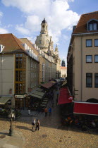 GERMANY, Saxony, Dresden, The restaurant and bar lined Munzgasse street with tourists leading to Neumarkt square and the Church of Our Lady Frauenkirche beyond in late afternoon light.