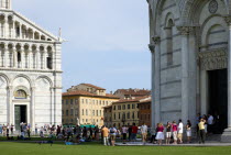 ITALY, Tuscany, Pisa, The Campo dei Miracoli or Field of Miracles.Touists on the grass between the Duomo Cathedral facade and the Baptistry entrance.