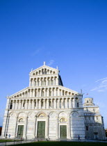 ITALY, Tuscany, Pisa, The Campo dei Miracoli or Field of Miracles with the Lombard style 12th Century facade of the Duomo Cathedral church and the leaning Tower beyond under a blue sky.
