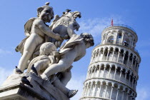 ITALY, Tuscany, Pisa, Campo dei Miracoli or Field of Miracles Marble statue of three cherubs holding a shield in front of the Leaning Tower belltower or Torre Pendente under a blue sky.