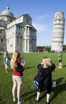 ITALY, Tuscany, Pisa, Campo dei Miracoli or Field of Miracles Tourists in front of the Duomo Cathedral and Leaning Tower belltower or Torre Pendente photographing each other pretending to hold the tow...