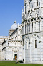 ITALY, Tuscany, Pisa, Campo dei Miracoli or Field of Miracles The Duomo Cathedral and Baptistry under a blue sky with tourist walking at their base.