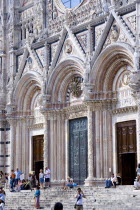 ITALY, Tuscany, Siena, Tourists on the steps of the pink black and white marble facade of the 13th Century Gothic Duomo Cathedral church of Santa Maria Assunta.