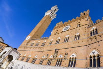 ITALY, Tuscany, Siena, The Torre del Mangia campanile belltower and facade of the Palazzo Publico town hall in the Piazza del Campo under a blue sky. The black and white crest or symbol of Siena decor...