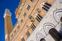 ITALY, Tuscan, Siena, The Torre del Mangia campanile belltower and facade of the Palazzo Publico town hall in the Piazza del Campo under a blue sky. The black and white crest or symbol of Siena decora...