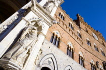 ITALY, Tuscany, Siena, Religious carvings on the portico entrance and facade of the Palazzo Publico town hall in the Piazza del Campo under a blue sky. The black and white crest or symbol of Siena dec...