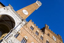 ITALY, Tuscany, Siena, Religious carvings on the portico entrance below the Torre del mangia campanile belltower and facade of the Palazzo Publico town hall in the Piazza del Campo under a blue sky. T...
