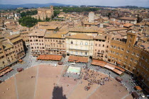 ITALY, Tuscany, Siena, Shadow of the Torre del Mangia campanile belltower in the Piazza del Campo with surrounding buildings and rooftops and the countryside beyond and the square busy with tourists.