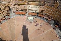 ITALY, Tuscany, Siena, Shadow of the Torre del Mangia campanile belltower in the Piazza del Campo with surrounding buildings and the square busy with tourists.