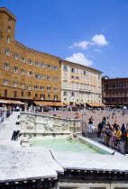 ITALY, Tuscany, Siena, Tourists around the 19th Century replica of the 15th Century white marble Fonte Gaia fountain by the artist Jacopo della Quercia in the Piazza del Campo with the square beyond.