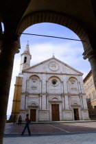 ITALY, Tuscany, Pienza, Val D'Orcia The Duomo in Piazza Pio II seen through an arch with tourists walking in the square. Built in 1459 by the architect Rossellino for Pope Pius II.