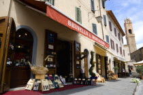 ITALY, Tuscany, Montalcino, Val D'Orcia Brunello di Montalcino Enoteca or wine shop with dispaly of boxed wines on the pavement around its entrance beneath a sunshade. The 14 the Century belltower of...