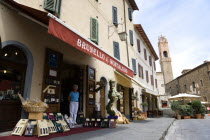 ITALY, Tuscany, Montalcino, Val D'Orcia Brunello di Montalcino Enoteca or wine shop with dispaly of boxed wines on the pavement around its entrance beneath a sunshade. The 14 the Century belltower of...